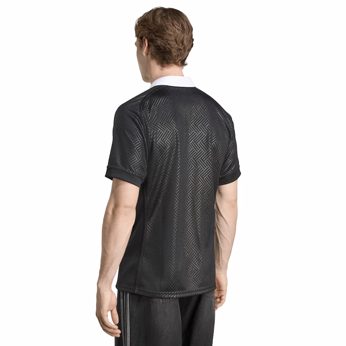 A man stands facing away, wearing the adidas Black Ferns WRWC25 Replica Home Jersey—a black short-sleeve shirt with a subtle geometric pattern and a white collar by adidas.