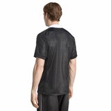 A man stands facing away, wearing the adidas Black Ferns WRWC25 Replica Home Jersey—a black short-sleeve shirt with a subtle geometric pattern and a white collar by adidas.