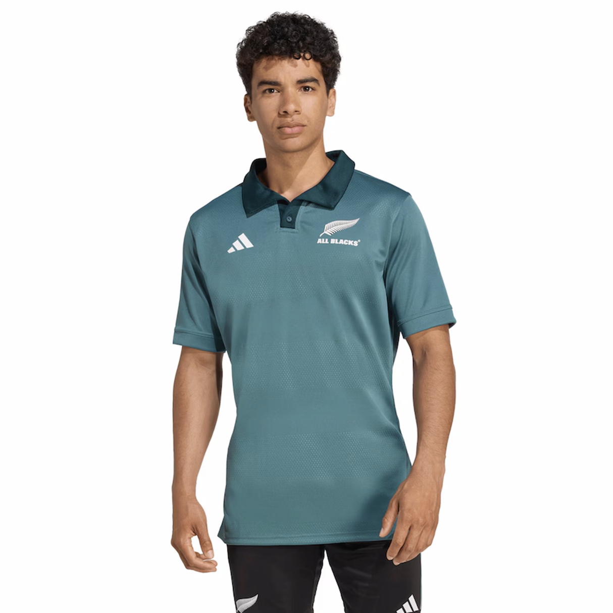 A young man wears the adidas All Blacks 25/26 Replica Training Jersey, featuring a teal color, black collar, and adidas logo, standing against a white background—perfect for showing your rugby pride.