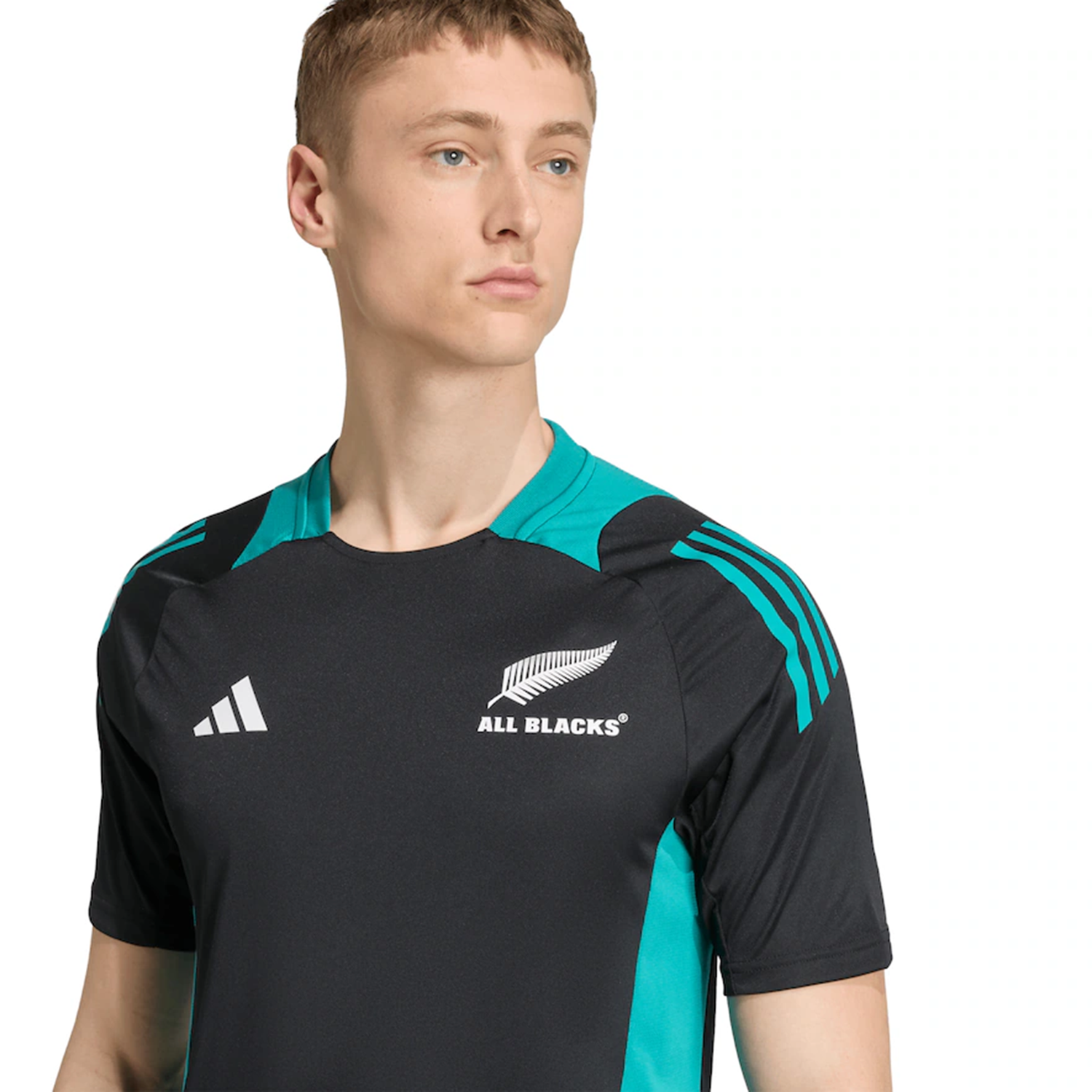 Someone wearing the adidas All Blacks 25/26 Performance T-Shirt in black and teal, featuring the logo, looks off to the side against a plain background.