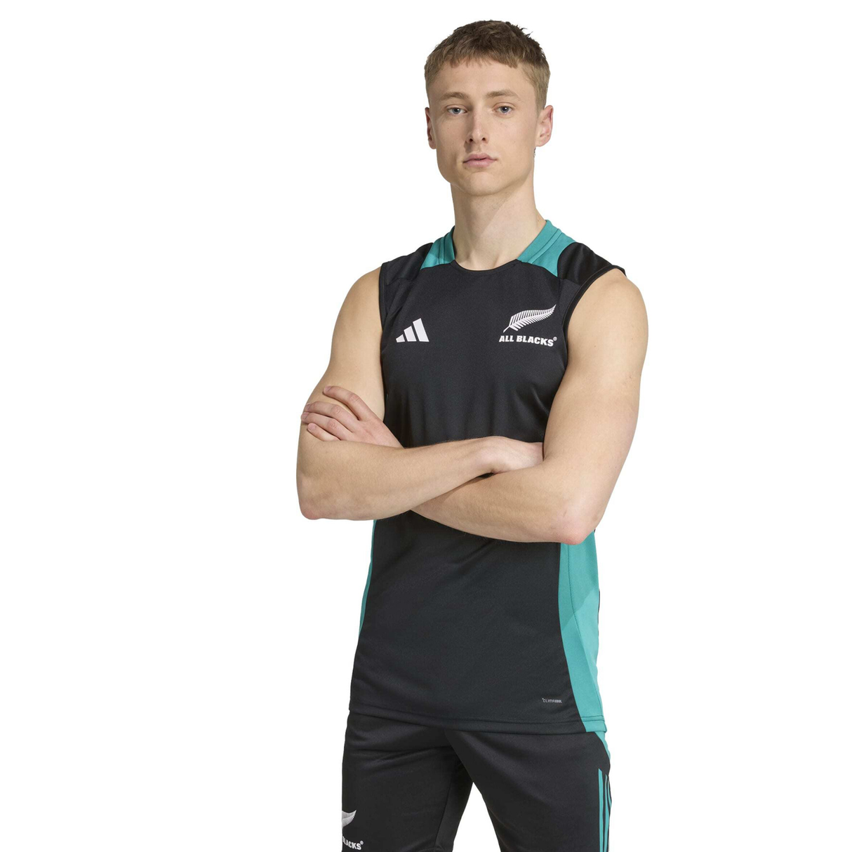 A man wears the adidas All Blacks 25/26 Training Singlet and matching shorts, standing with arms crossed against a white background—ideal attire for rugby training sessions.