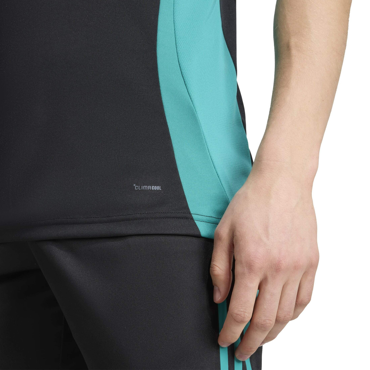 A person wears black athletic pants and the adidas All Blacks 25/26 Training Singlet in black and teal, with one hand by their side.