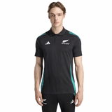 A person wears the All Blacks 25/26 Training Polo by adidas, a black training shirt with teal accents, standing against a plain background.