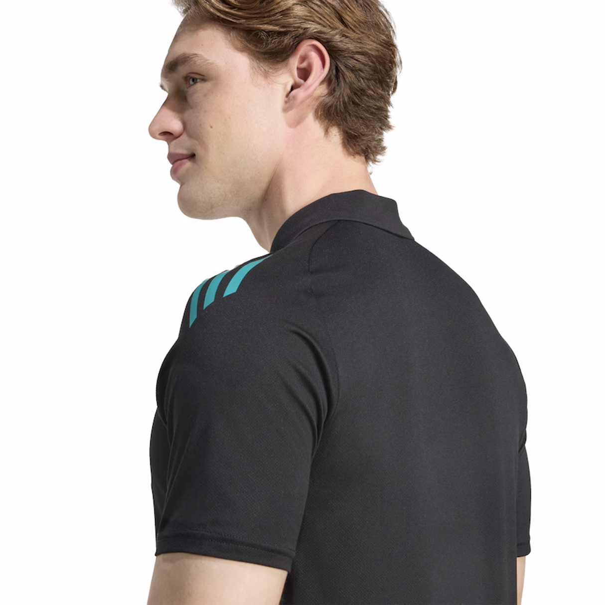 A man with light brown hair wears the All Blacks 25/26 Training Polo by adidas, black with teal shoulder stripes, shown from the side and rear against a white background.