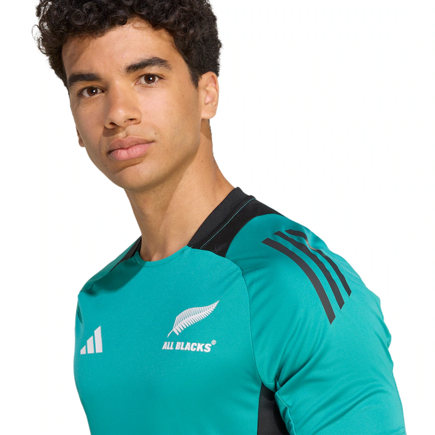 A person wearing the teal All Blacks 25/26 Performance T-Shirt by adidas with black accents and logos, looking at the camera against a plain background.