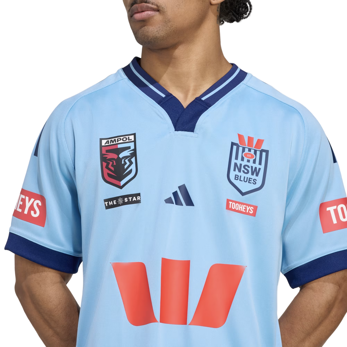 A person wearing the New South Wales Blues 25/26 Replica Home Jersey by adidas, in light blue, featuring sponsor logos like Ampol, Tooheys, The Star, and classic adidas rugby detailing.