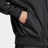 Wearing the Originals Limited Edition All Blacks Firebird Track Top by adidas, they have a hand in the side pocket, highlighting the iconic adidas logo. Made from recycled polyester, this black jacket combines style and sustainability.