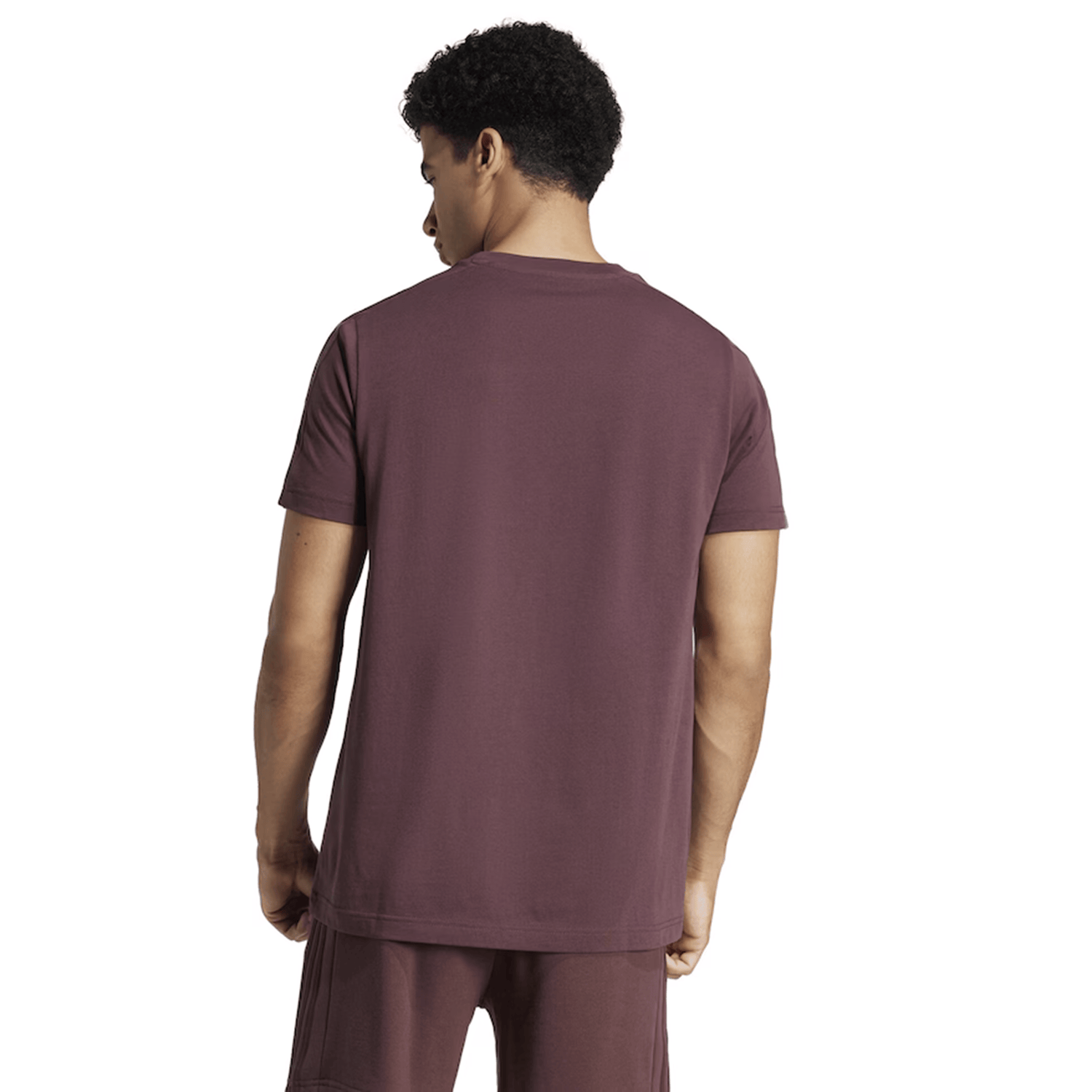 Wearing the All Blacks 24/25 Fan Tee by adidas, the individual turns, subtly revealing the iconic adidas 3-Stripes adorning their maroon t-shirt and shorts.