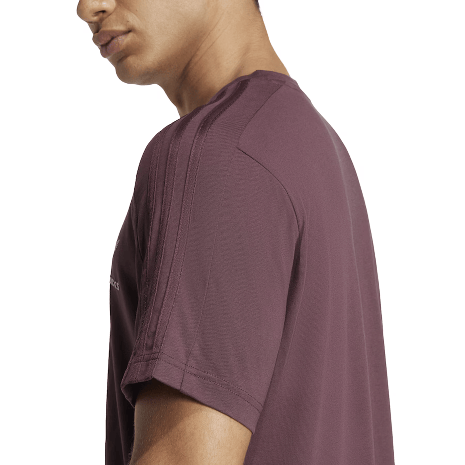 The person is wearing the All Blacks 24/25 Fan Tee by adidas in maroon, made from cozy single jersey fabric, revealing a side view of their upper body.