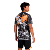 A man faces away, wearing the adidas All Blacks 26/27 Captains Run Replica Jersey with striking orange and white graphic details, paired with black shorts featuring an orange stripe.