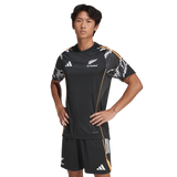 A man stands hands on hips in an adidas All Blacks 26/27 Marvel Performance Training Tee and shorts against a plain background.
