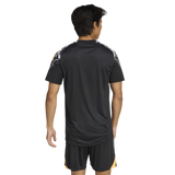 A person stands facing away, wearing the adidas All Blacks 26/27 Marvel Performance Training Tee and black shorts with yellow accents, set against a plain white background.