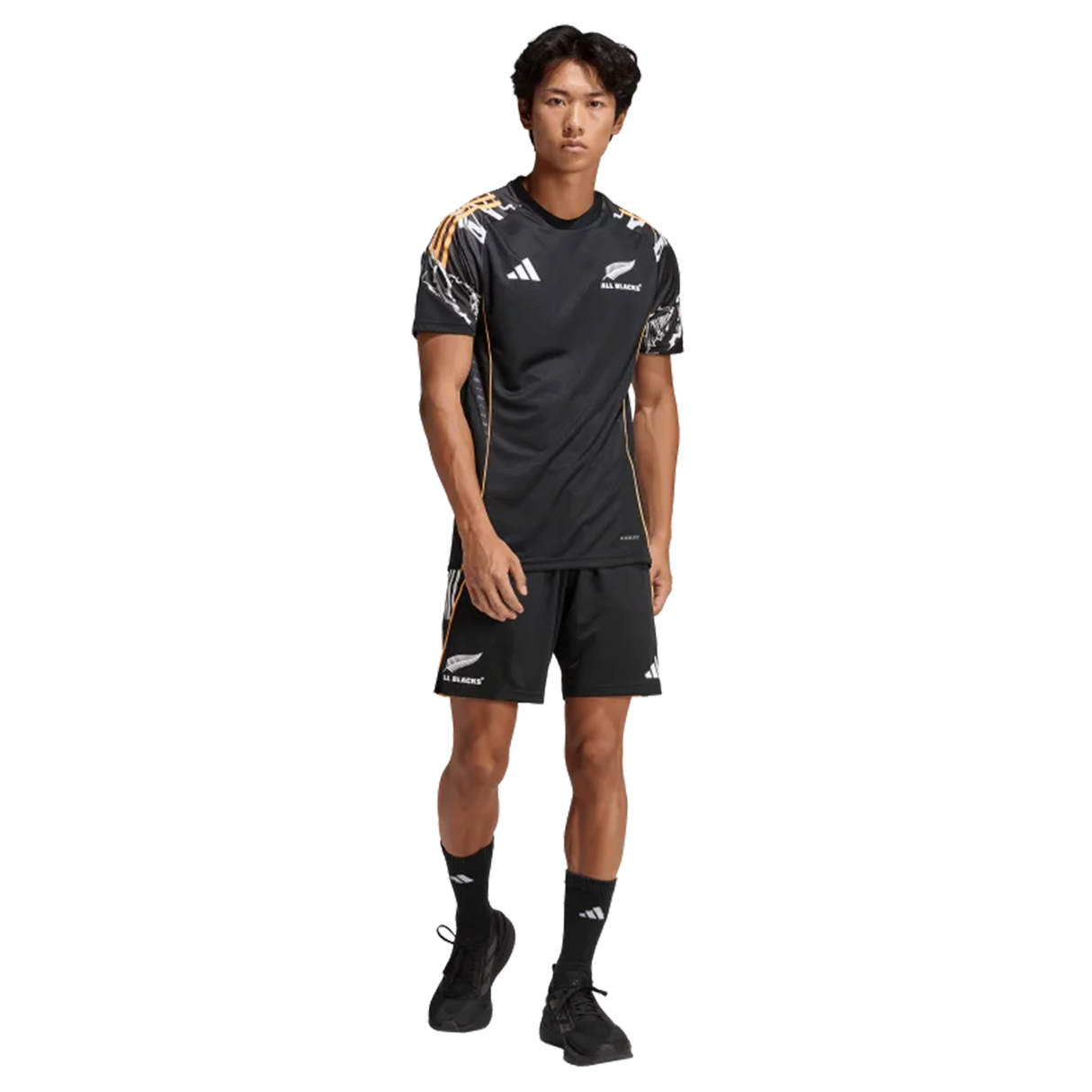 A man stands facing forward wearing a black adidas All Blacks 26/27 Marvel Performance Training Tee with logos and patterned shoulder accents, paired with matching shorts.