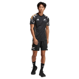 A man stands facing forward wearing a black adidas All Blacks 26/27 Marvel Performance Training Tee with logos and patterned shoulder accents, paired with matching shorts.