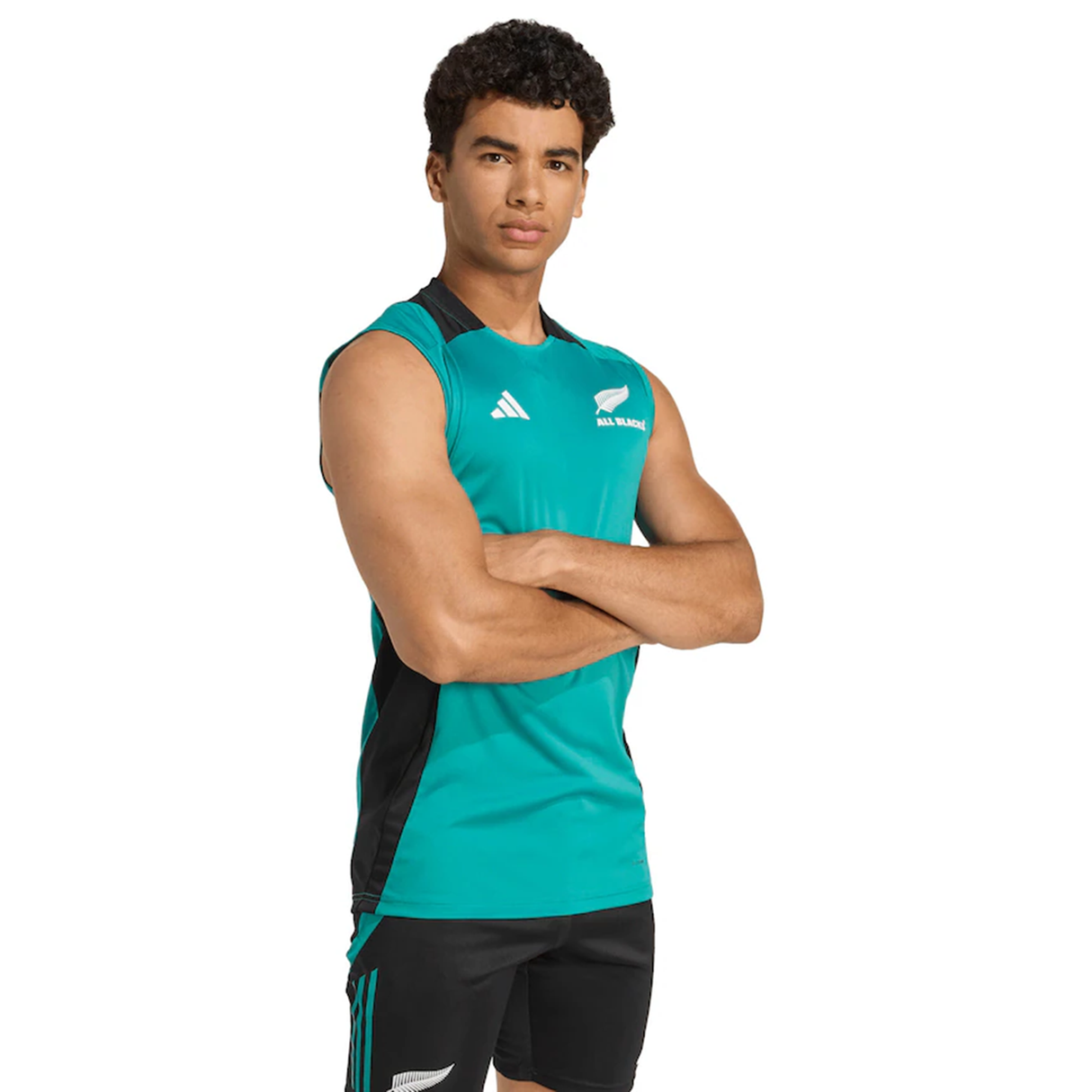 A person stands arms crossed, wearing the adidas All Blacks 25/26 Training Singlet and matching shorts with sports logos, facing forward against a white background—ideal for rugby training.