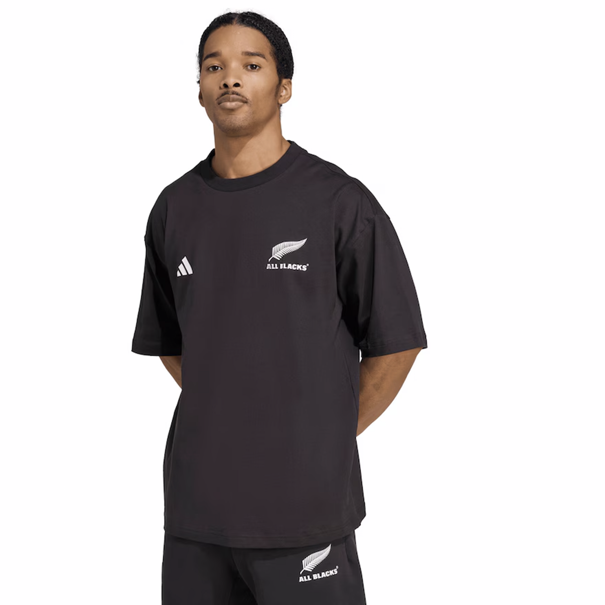 A person in the adidas All Blacks 25/26 Presentation T-Shirt stands facing forward, hands behind their back. The shirt features the iconic silver fern, representing the All Blacks.