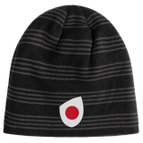 The EMB Canterbury Japan Shield Beanie sports a bold black and gray striped pattern, accented by a prominent red and white circular logo on the front.