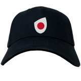 A sleek EMB Canterbury Japan Shield Flex Drill Cap in black, featuring a distinctive white and red emblem on the front.