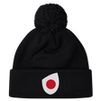 The Japan Shield Pom Pom Beanie by EMB Canterbury is black and features a unique logo of a red dot inside a white teardrop shape on the cuff, similar to the Japan Shield.