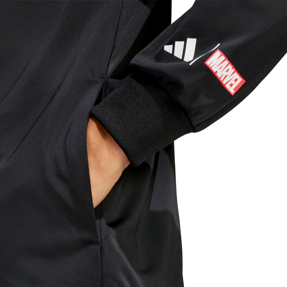 A hand is in the pocket of black pants. The black sleeve, from the adidas All Blacks 26/27 Marvel Track Top, features adidas stripes and a red Marvel logo patch for a bold, Marvel-inspired sportswear style.