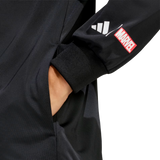 A hand is in the pocket of black pants. The black sleeve, from the adidas All Blacks 26/27 Marvel Track Top, features adidas stripes and a red Marvel logo patch for a bold, Marvel-inspired sportswear style.