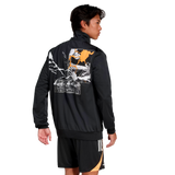 A man stands facing away in the All Blacks 26/27 Marvel Track Top by adidas, showcasing its bold graphic back design, paired with black shorts with orange and white accents for a striking Marvel-inspired sportswear look.