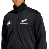 A person wearing the All Blacks 26/27 Marvel Track Top by adidas—a black zip-up jacket featuring the adidas logo and silver fern emblem, ideal rugby fan apparel.