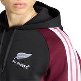 Wearing the adidas All Blacks 27/28 Hoodie in black and maroon, featuring iconic white sleeve stripes and a silver fern “ALL BLACKS” logo on the chest, this person proudly supports New Zealand rugby.