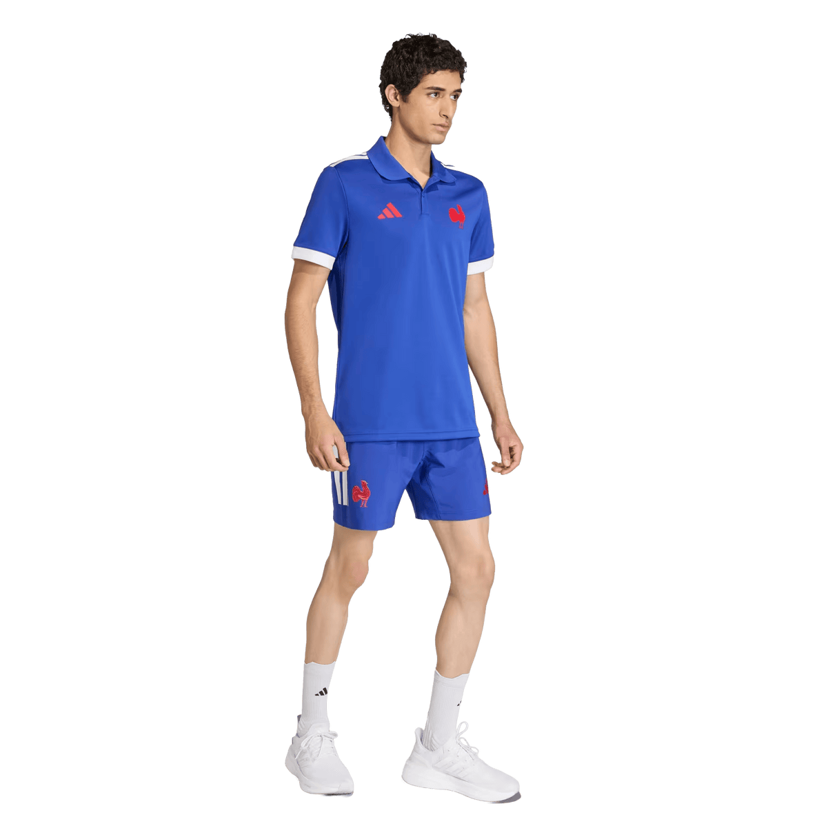 A man wears the adidas France FFR Home Supporters Replica Polo with matching shorts featuring red logos, white socks, and white athletic shoes against a plain background—ideal for passionate France Rugby fans.