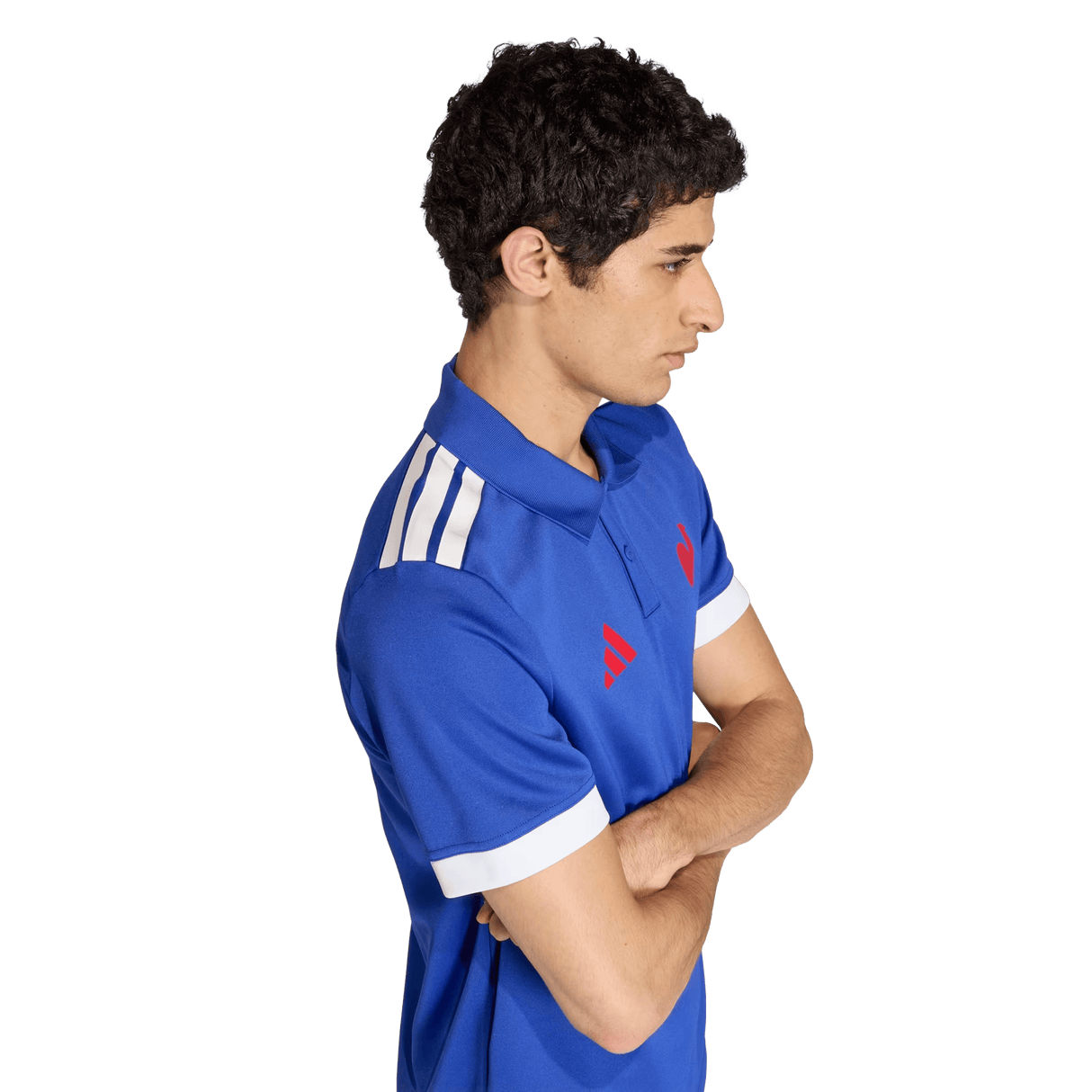 A person stands in profile, arms crossed, wearing the France FFR Home Supporters Replica Polo by adidas—featuring white shoulder stripes and red logos—displaying pride as a France FFR fan.