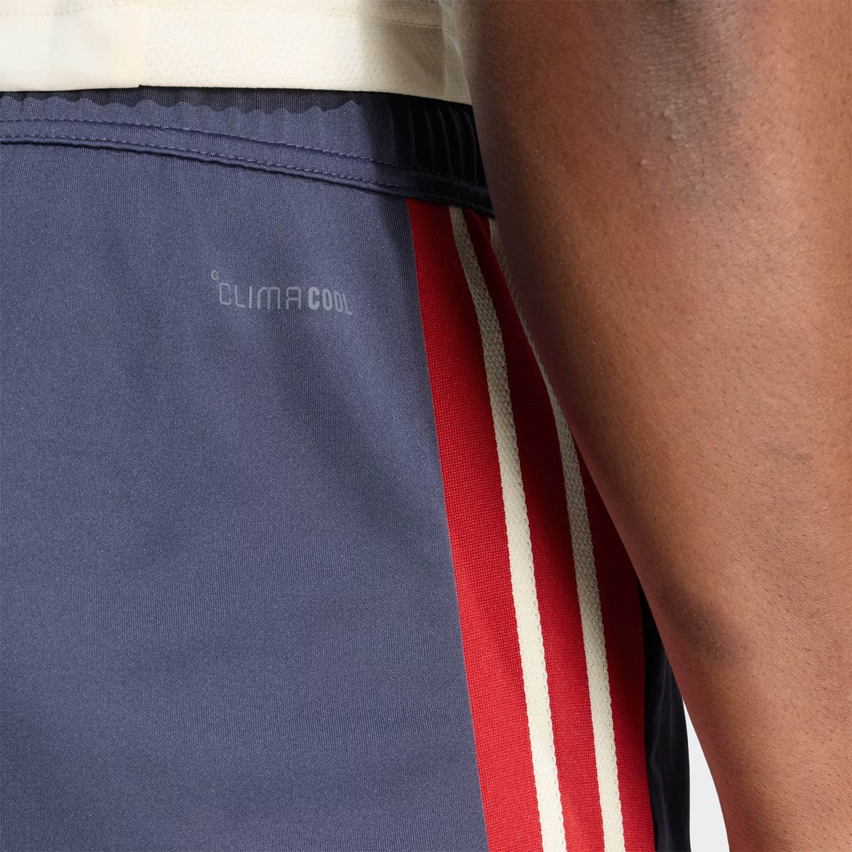 Close-up of a person wearing the France FFR 26/27 Gym Short by adidas, featuring navy fabric with red and white stripes and “ClimaCool” text, showing part of their arm and shirt.