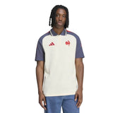 A person wearing the France FFR 26/27 Training Polo by adidas—a short-sleeve cream and navy rugby shirt with red chest logos—paired with blue jeans, standing against a white background.