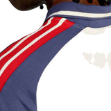 Close-up of a person’s shoulder wearing the France FFR 26/27 Training Polo by adidas, featuring blue fabric with red and white stripes on the sleeve—a part of the official adidas training polo collection for the French Rugby Federation.