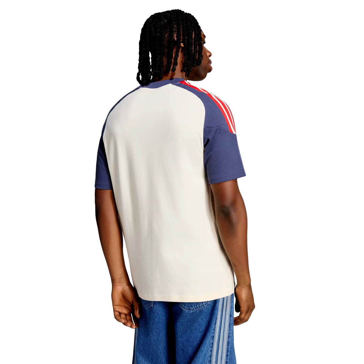 A man is seen from behind wearing the France FFR 26/27 Cotton T-Shirt by adidas, featuring a beige back, navy short sleeves, and red shoulder stripes, paired with blue jeans.