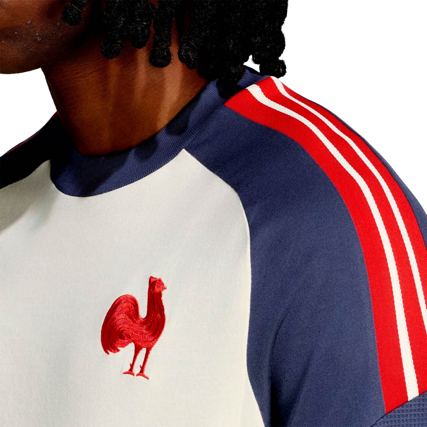 A person wearing the France FFR 26/27 Cotton T-Shirt by adidas, featuring a white and blue design with red shoulder stripes and the iconic Le Coq badge—a bold red rooster emblem—on the chest.