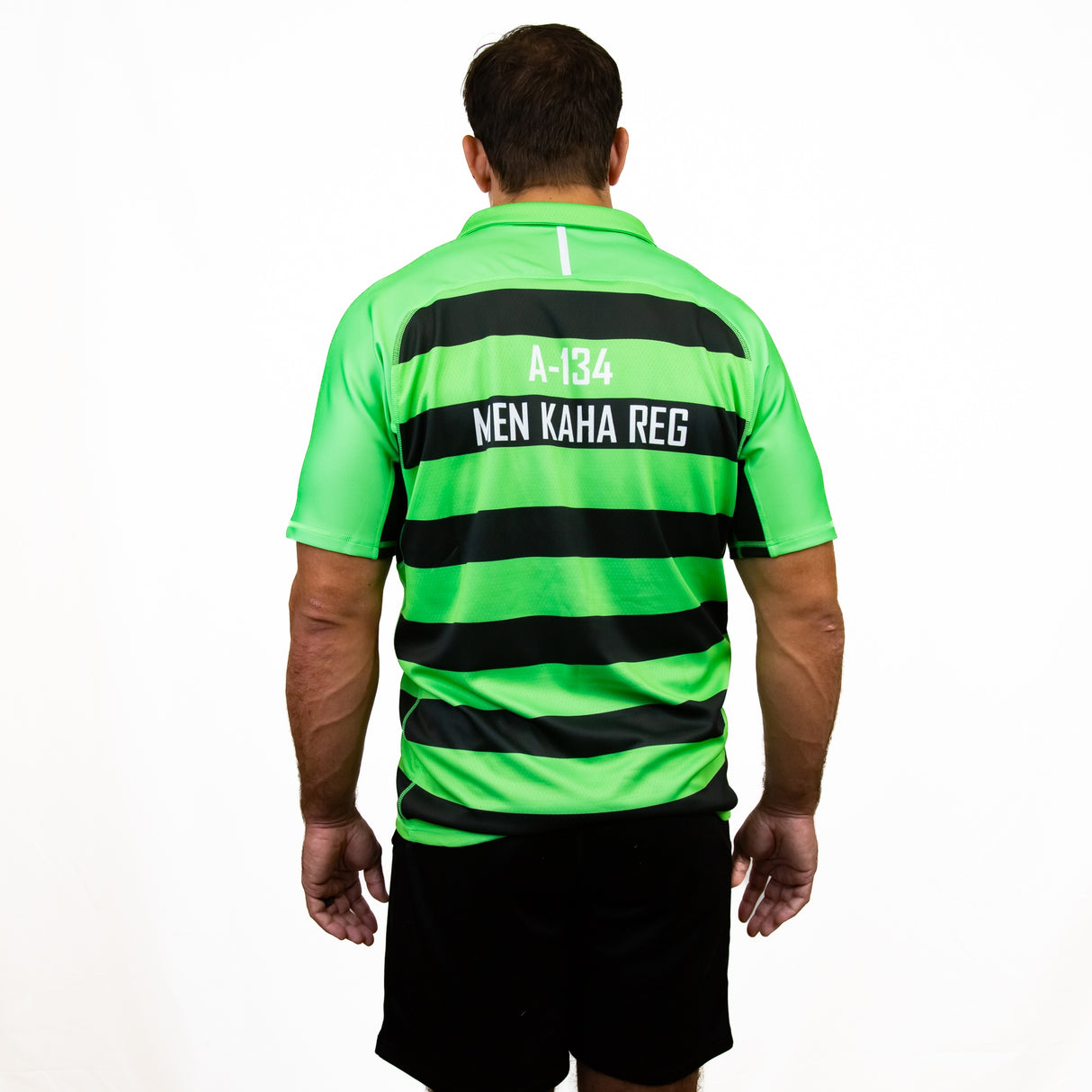A man faces away, wearing the Teamatical Canterbury Elite Full Custom Sublimated Jersey - Mens in green and black stripes with “A-134 NEN KAHA REG” on the back, set against a plain white background.