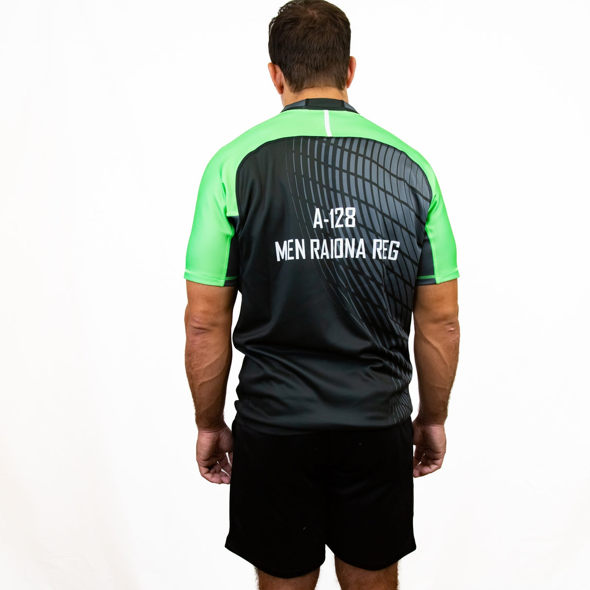 A man faces away from the camera wearing a black and green Teamatical Canterbury Elite Full Custom Sublimated Jersey - Mens, with "A-128 MEN RAIONA REG" printed on the back, paired with black shorts.