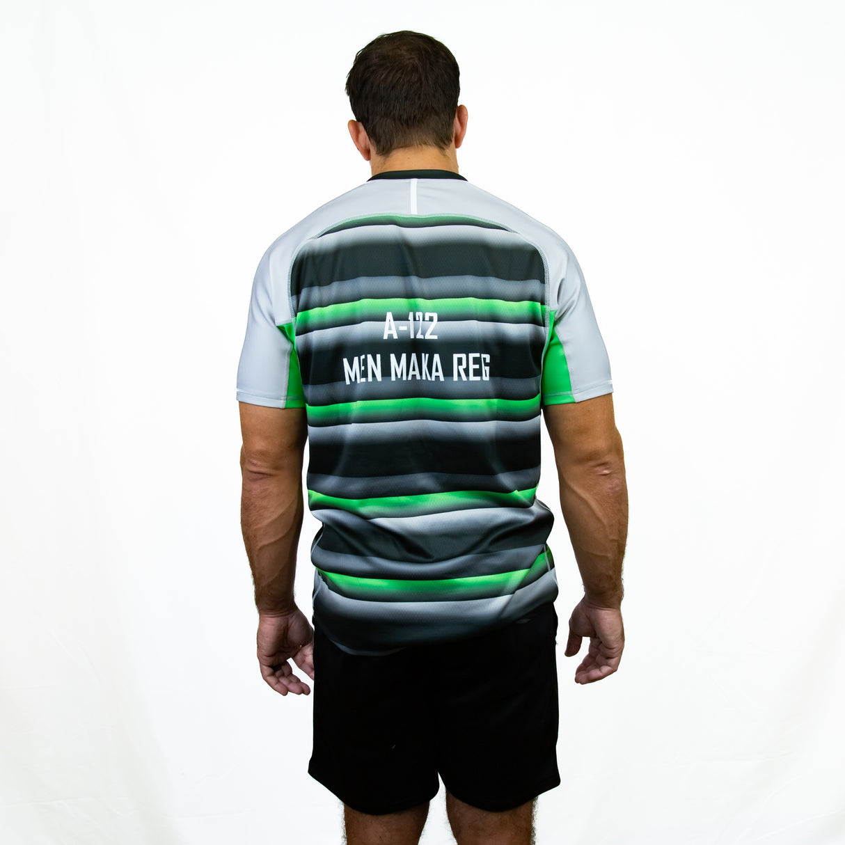 A man faces away, wearing the Teamatical Canterbury Elite Full Custom Sublimated Jersey - Mens with green, gray, and black stripes, paired with black shorts against a plain white background.