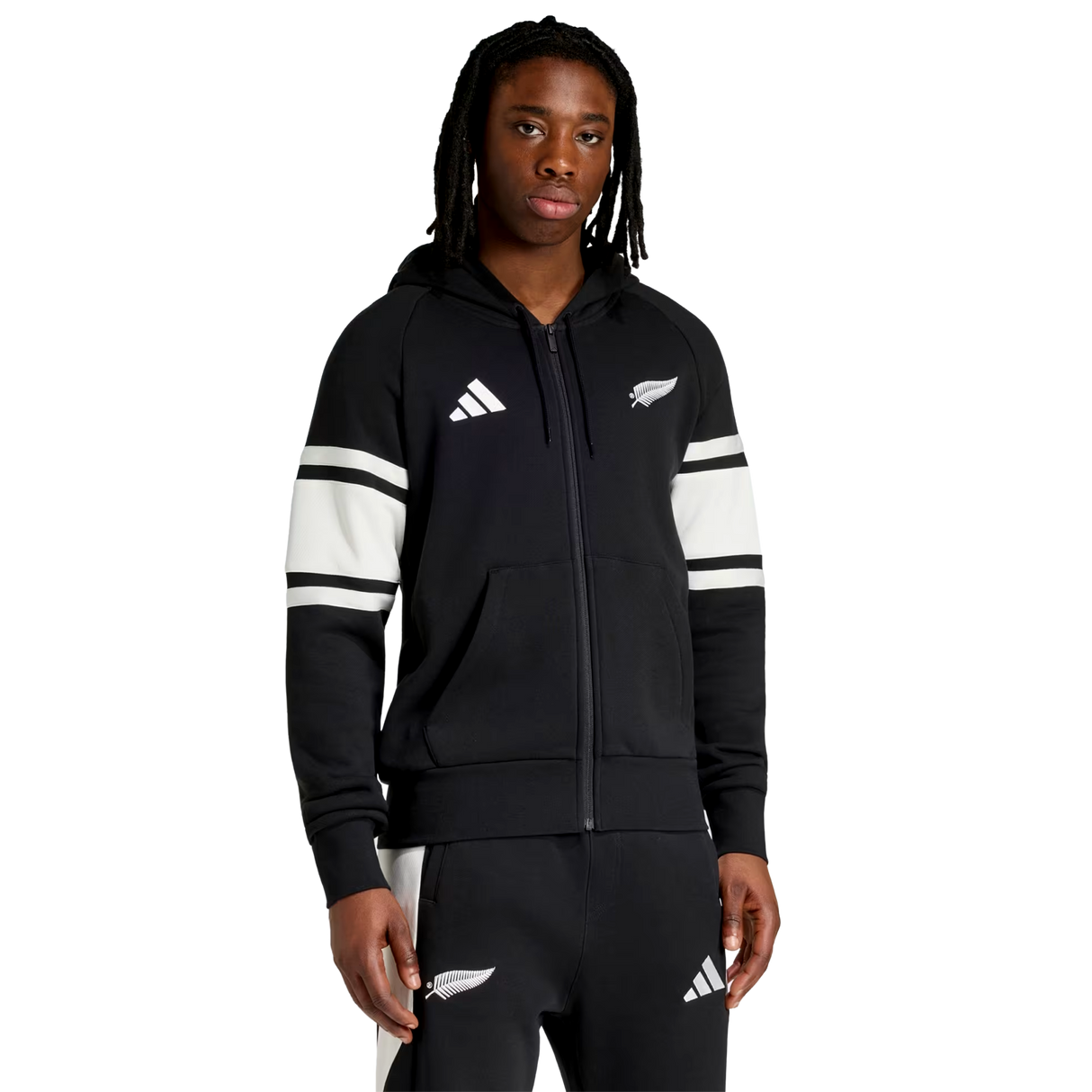 A person wears the All Blacks 26/27 Travel Full Zip Hoodie by adidas, featuring white stripes and sports logos, standing against a plain white background.