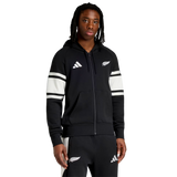 A person wears the All Blacks 26/27 Travel Full Zip Hoodie by adidas, featuring white stripes and sports logos, standing against a plain white background.