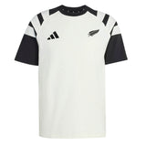 The All Blacks 26/27 Travel T-Shirt by adidas is a white and black short-sleeve shirt featuring a striking black fern and the adidas logo on the chest, along with bold black angled stripes on the shoulders—a classic look inspired by the iconic New Zealand rugby shirt.