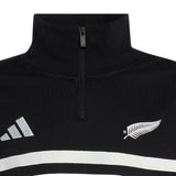 Close-up of the adidas All Blacks 26/27 Leisurewear 1/4 Zip Sweatshirt, a black pullover featuring a white fern emblem on the right and a white geometric logo on the left, with two white horizontal stripes below—an iconic piece of New Zealand Rugby leisurewear.