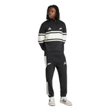 A person is wearing the All Blacks 26/27 Leisurewear 1/4 Zip Sweatshirt by adidas, styled with a black and white athletic tracksuit featuring adidas logos and stripes, paired with white adidas sneakers, standing against a white background.