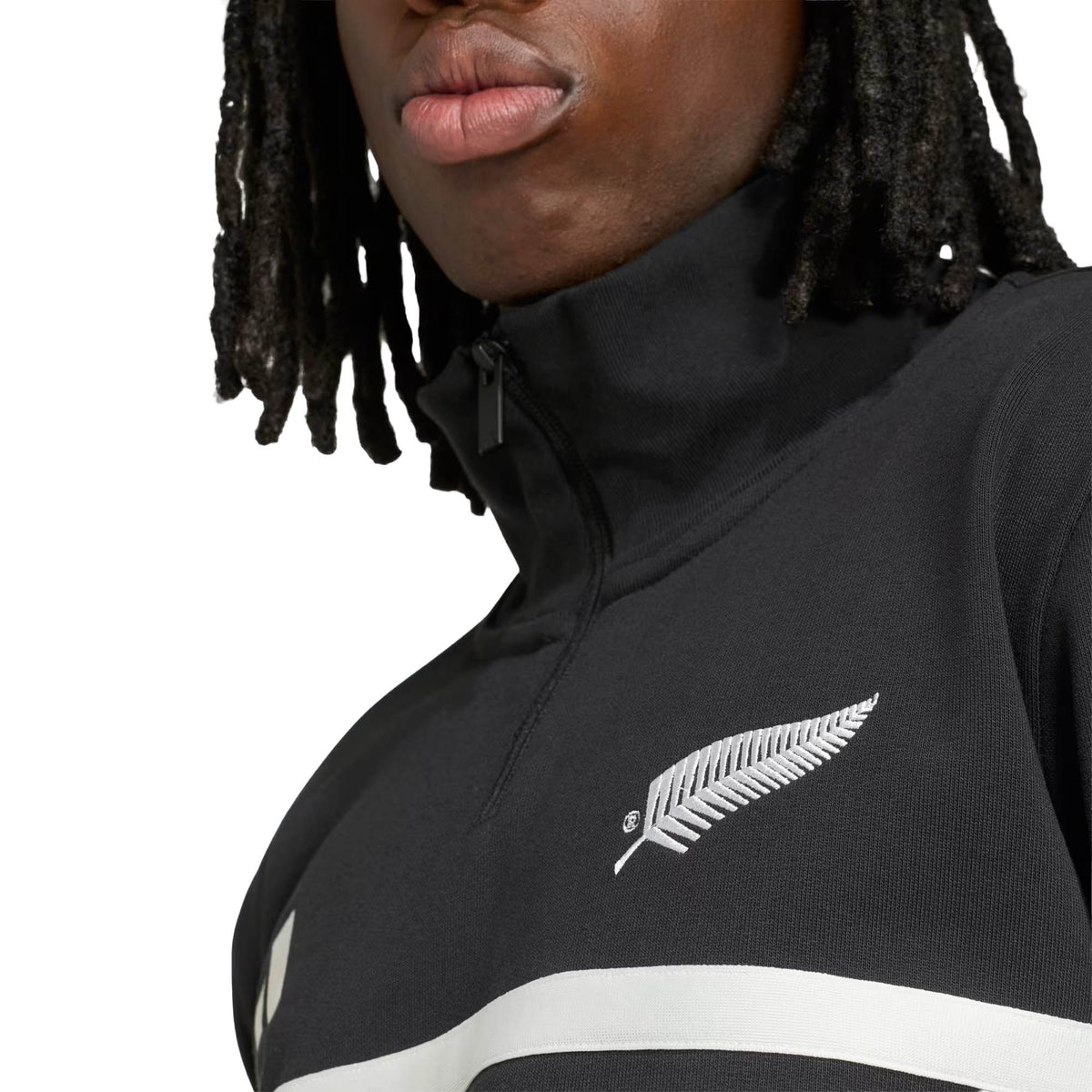 A person wearing the adidas All Blacks 26/27 Leisurewear 1/4 Zip Sweatshirt, featuring a white fern leaf emblem on the chest. Only the lower half of their face and upper torso are visible, highlighting this iconic piece of New Zealand Rugby apparel by adidas.
