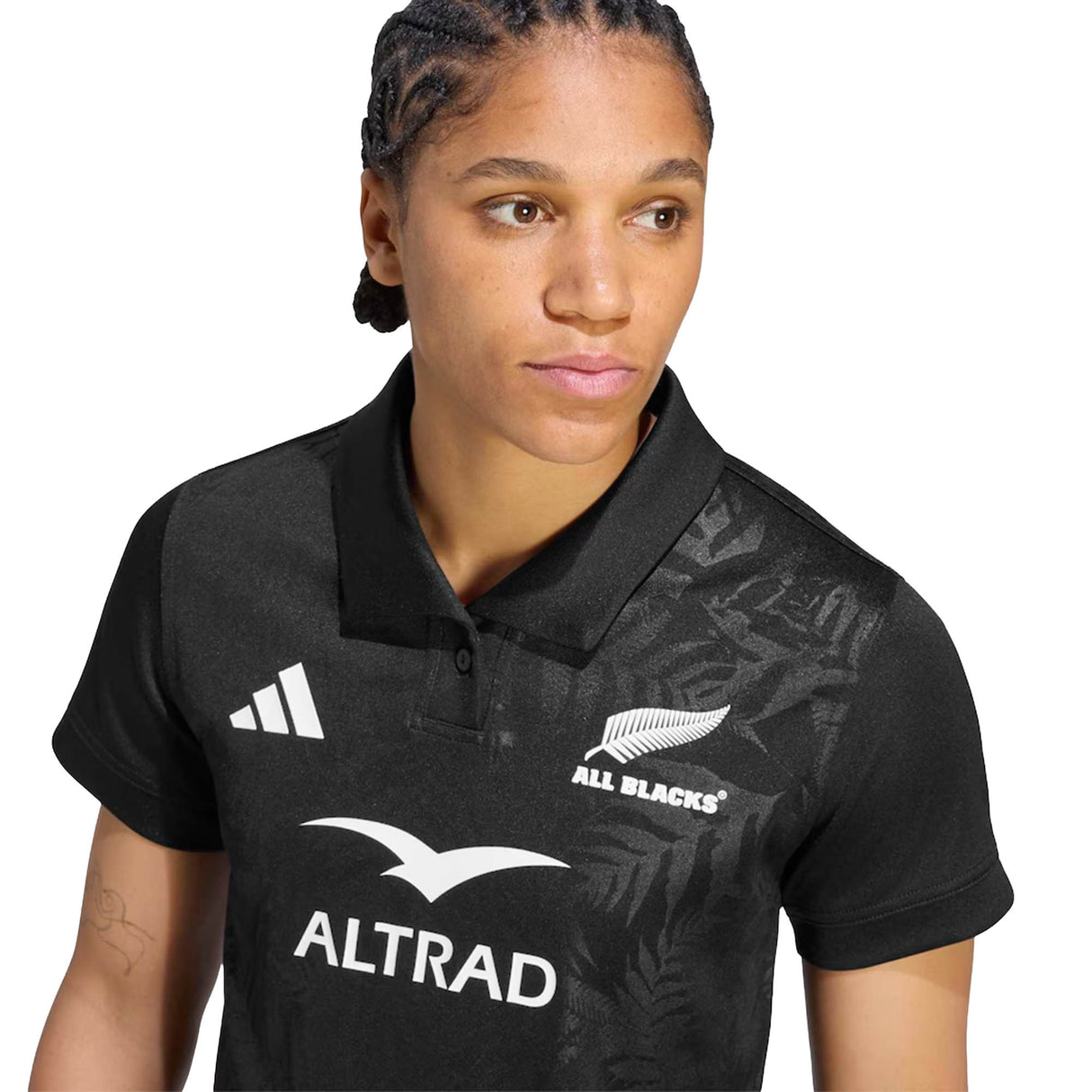 A person wearing the Women’s All Blacks Greatest Rivalry Replica Home Jersey by adidas—a black rugby polo shirt featuring the iconic adidas logo—looking slightly to the side.