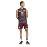 A person in the adidas All Blacks Greatest Rivalry Training Singlet and matching shorts stands with arms behind their back, wearing striped socks and black sneakers against a white background.
