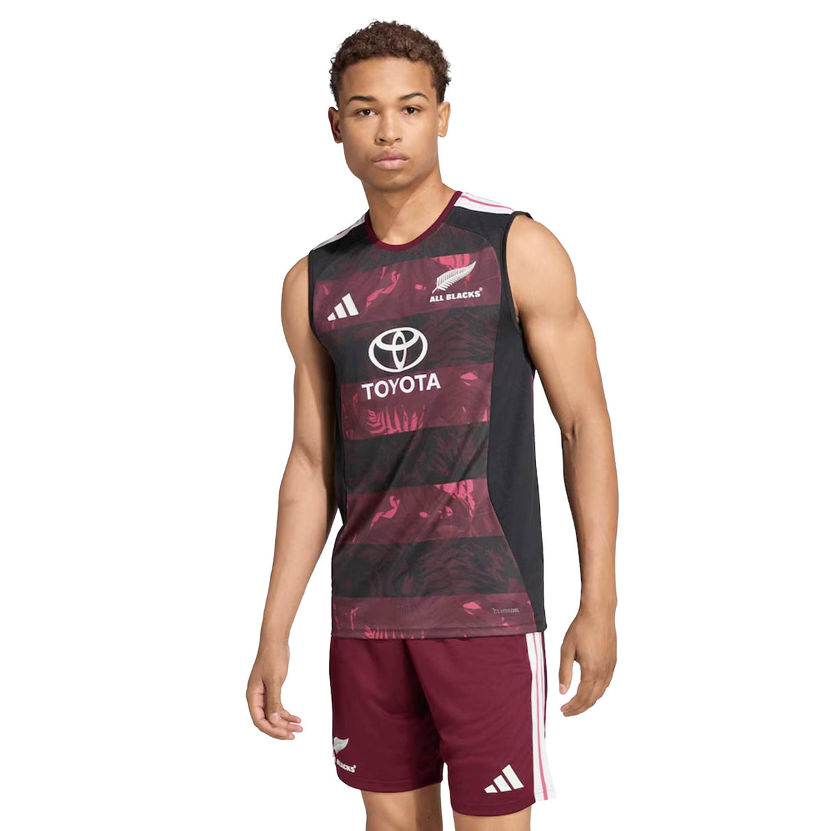A male model wears the All Blacks Greatest Rivalry Training Singlet by adidas—a sleeveless rugby performance top featuring Toyota and adidas logos—paired with maroon athletic shorts, standing against a white background. This look draws inspiration from the latest adidas South Africa tour collection.