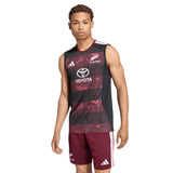A male model wears the All Blacks Greatest Rivalry Training Singlet by adidas—a sleeveless rugby performance top featuring Toyota and adidas logos—paired with maroon athletic shorts, standing against a white background. This look draws inspiration from the latest adidas South Africa tour collection.