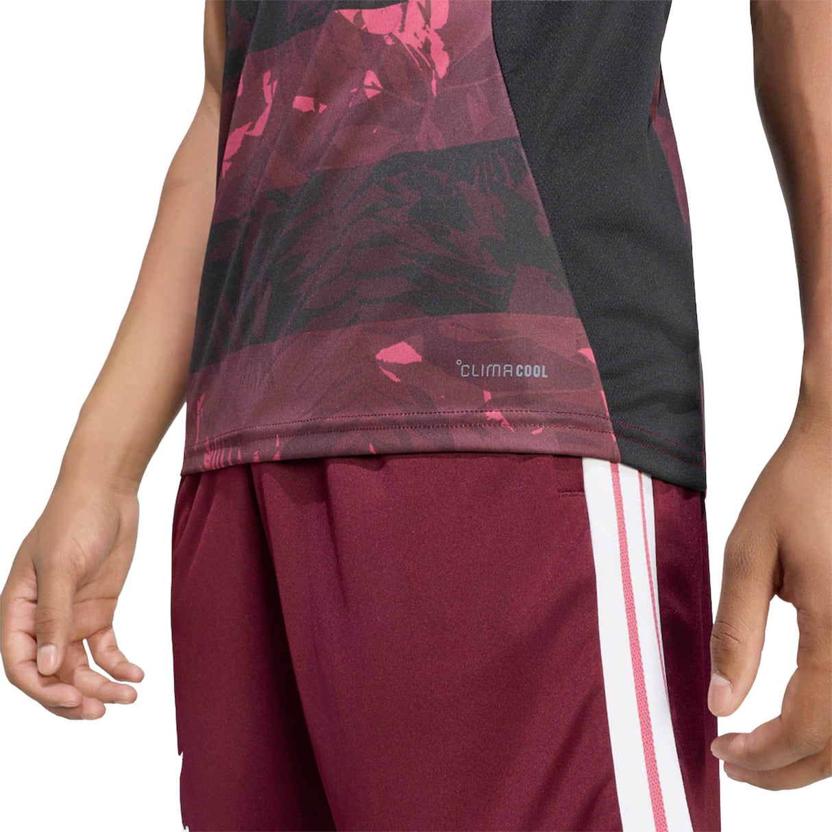 A person dressed in the adidas All Blacks Greatest Rivalry Training Singlet—a maroon and black sports top from adidas—paired with matching maroon shorts featuring white stripes, shown from chest to thighs.