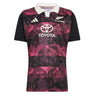 Introducing the All Blacks 26/27 Training Jersey - South Africa Tour by adidas: a short-sleeve rugby jersey featuring a crisp white collar, bold black sleeves, and an eye-catching pink and purple leaf pattern. This adidas design displays the All Blacks, adidas, and Toyota logos on the front and is crafted as an official training jersey inspired by the All Blacks’ tour of South Africa.